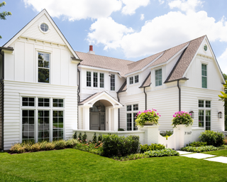 Home exterior painted in fresh ivory color, with greenery in borders around lawn and colorful planting on entrance