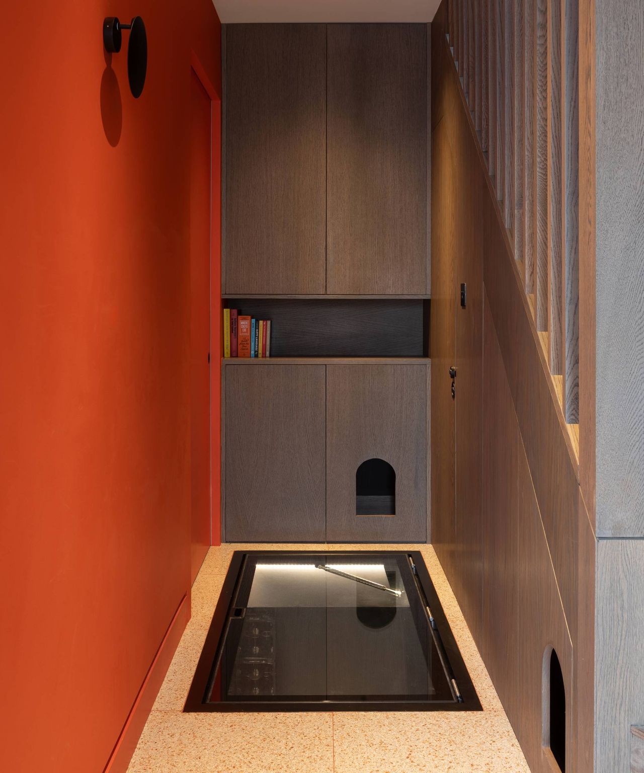 hallway with glass floor panel to wine cellar, orange wall and built in joinery in timber