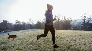 Gut health in winter - woman running in a field with her dog