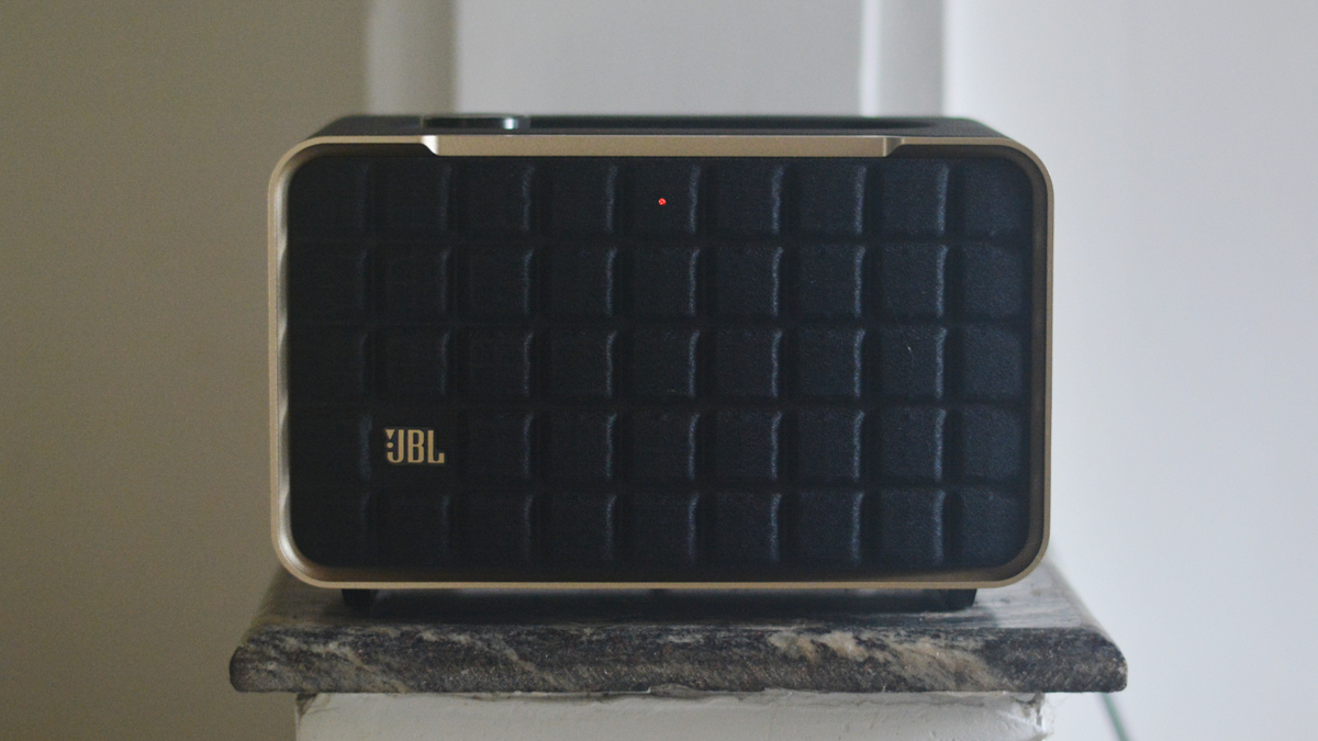 The JBL Authentics 200 speaker on a sits on a small marble surface. We can see its front grille clearly, which is divided into embossed squares with a silver surround, in a retro style