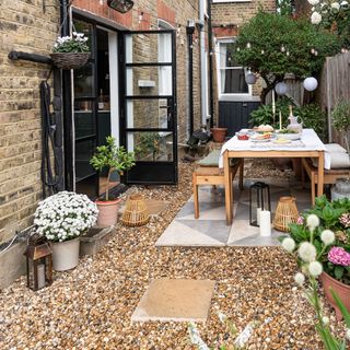 Narrow courtyard garden covered in gravel and tiles, with dining table and benches