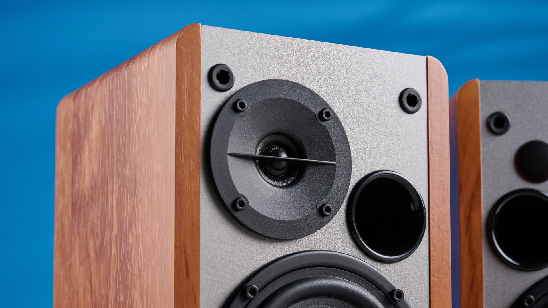 the edifier r1280t bookshelf speakers in wood brown photographed against the blue background, showing the volume adjustment dials, internal drivers and tweeters, RCA and aux inputs, and remote