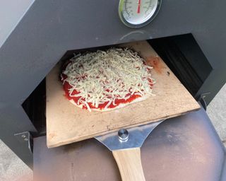Outsunny Outdoor Garden Pizza Oven Charcoal BBQ putting the pizza in the oven