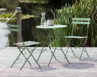 A green metal bistro set on the boardwalk overlooking a lake