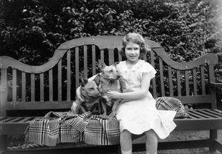Princess Elizabeth sitting on a garden seat with two corgi dogs at her home on 145 Piccadilly, London.