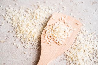 Close-up of raw white rice in a wooden spoon and on a table.