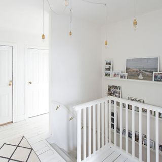 bright white landing area with shelves with family photos and a statement ceiling light with exposed bulbs