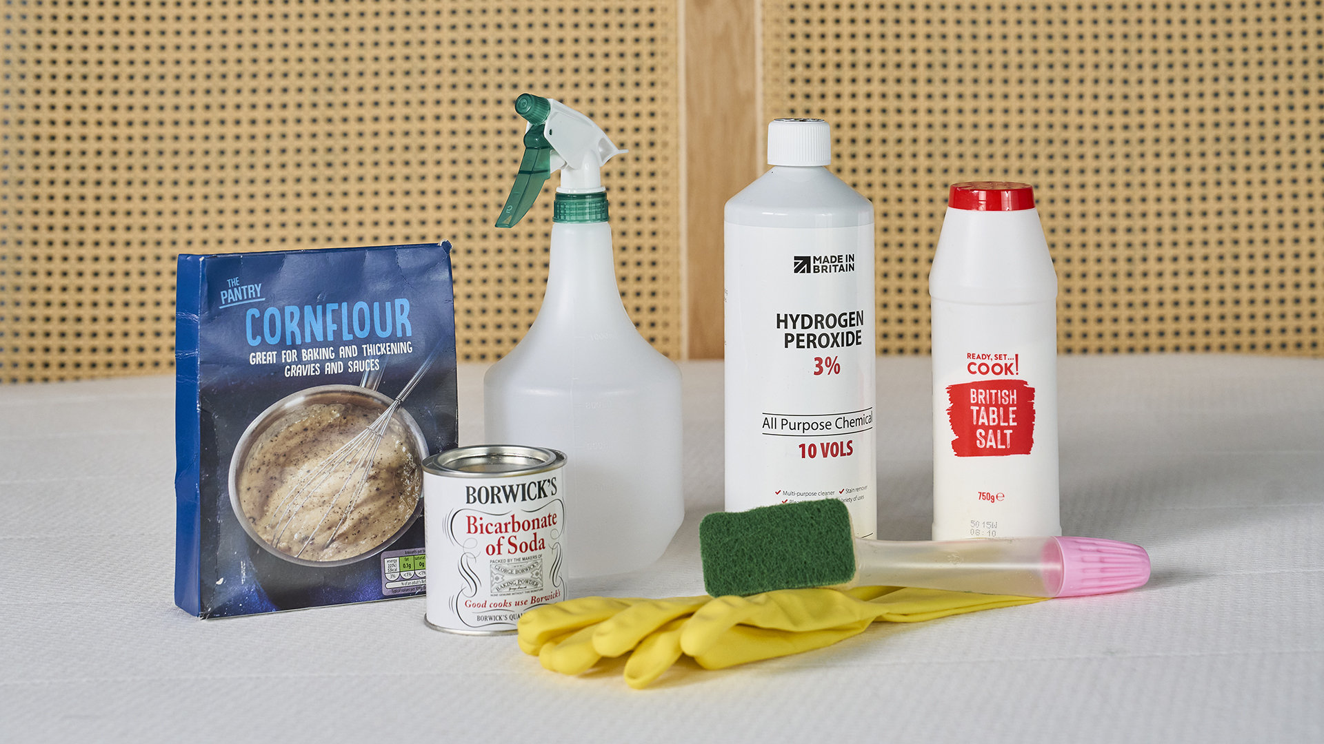 Hydrogen peroxide, salt, bicarbonate of soda, cornflour, a spray bottle and washing up gloves sitting on a bed