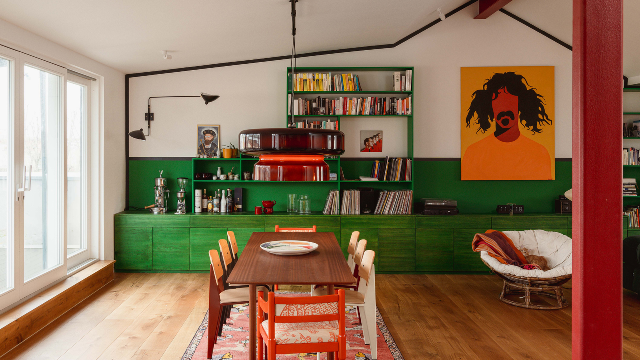 Bright open plan kitchen diner with green cabinets, wooden table and yellow artwork on the wall