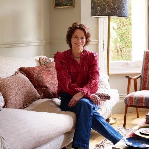 Image of a woman in a red top and jeans sitting on a light pink couch in a beige room.
