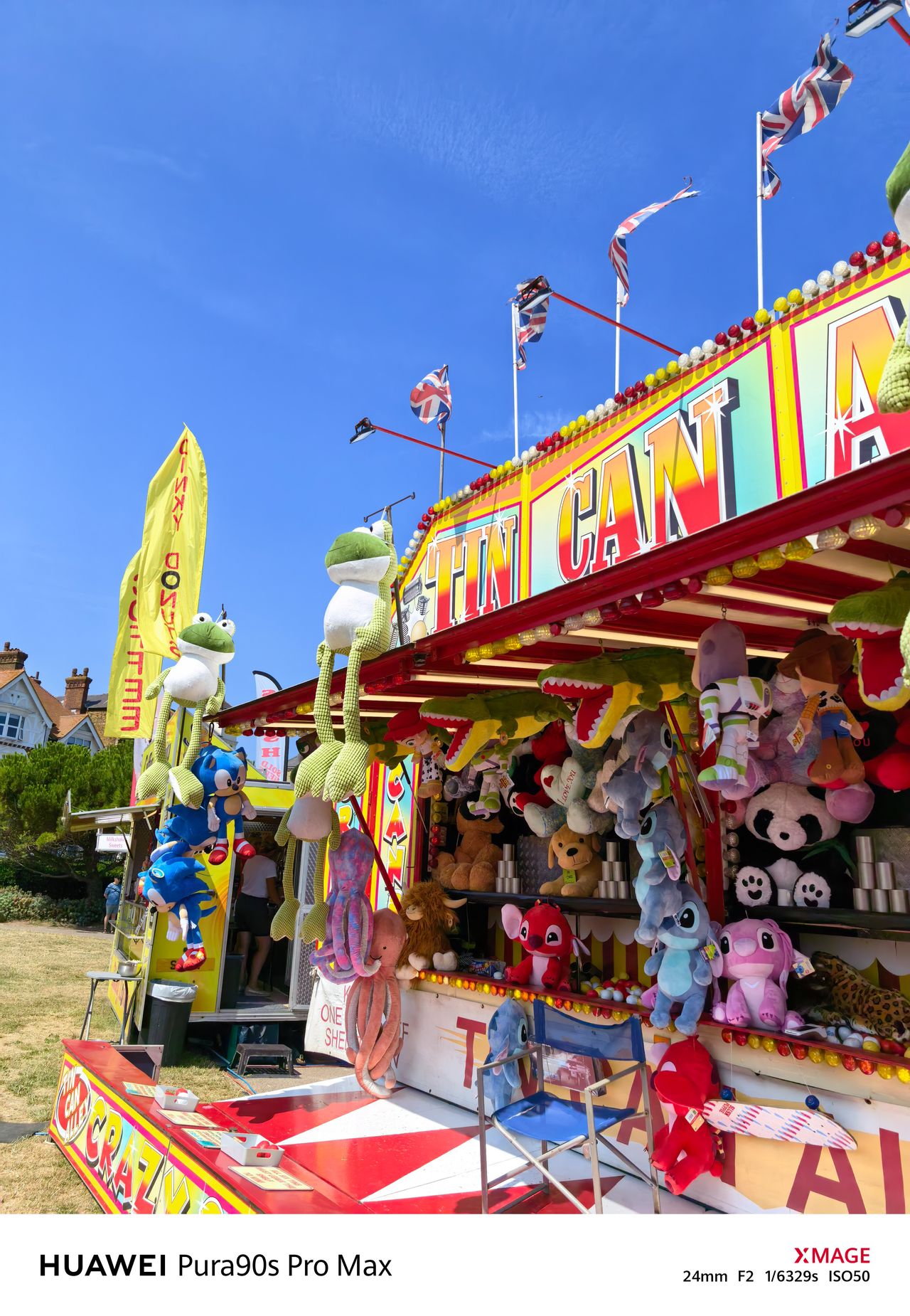 Colorful fairground tin-can game stall filled with hanging plush prizes and Union Jack flags.