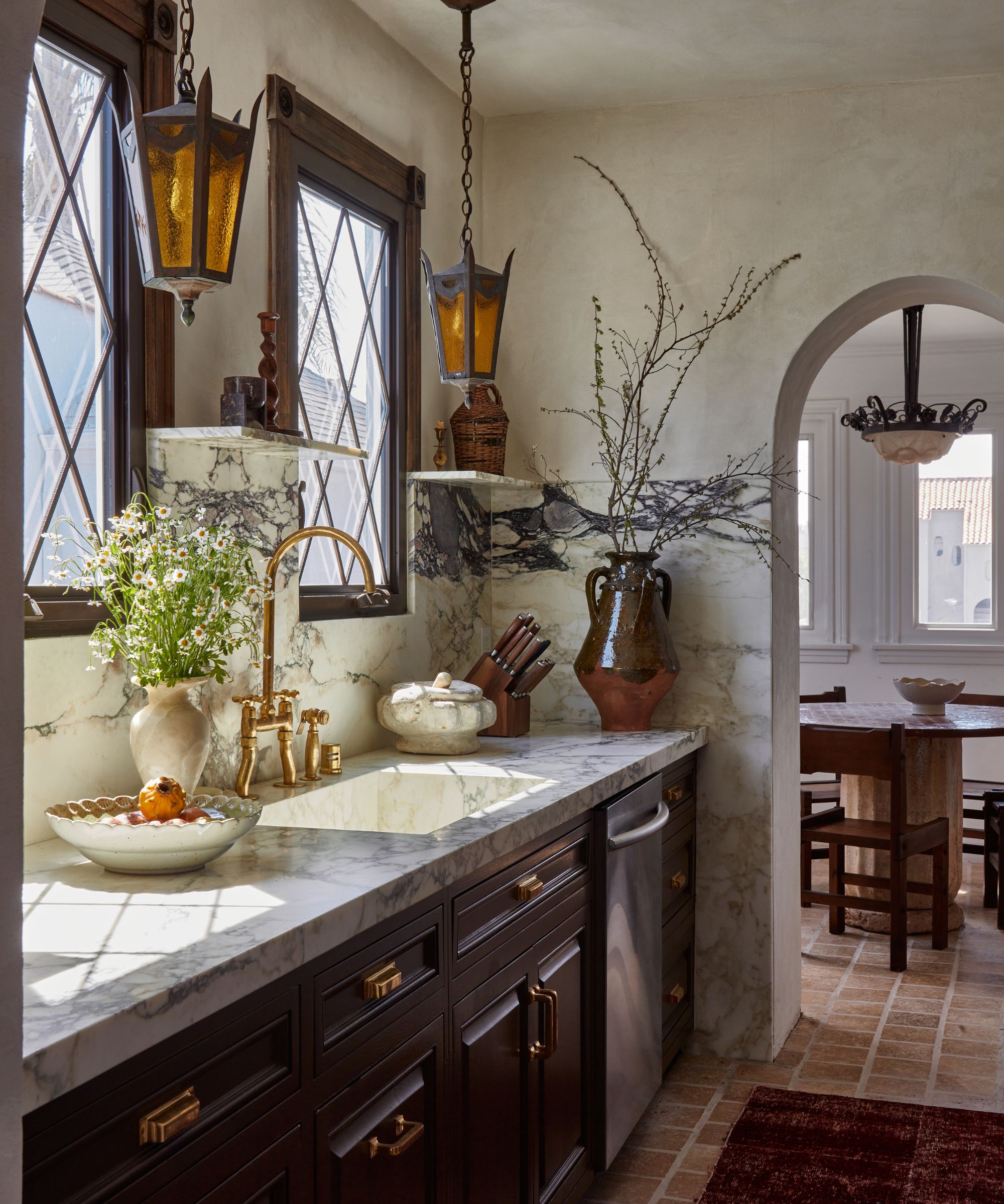 A Spanish revival kitchen with brown cabinets and marble for the countertops, sink, and backsplash