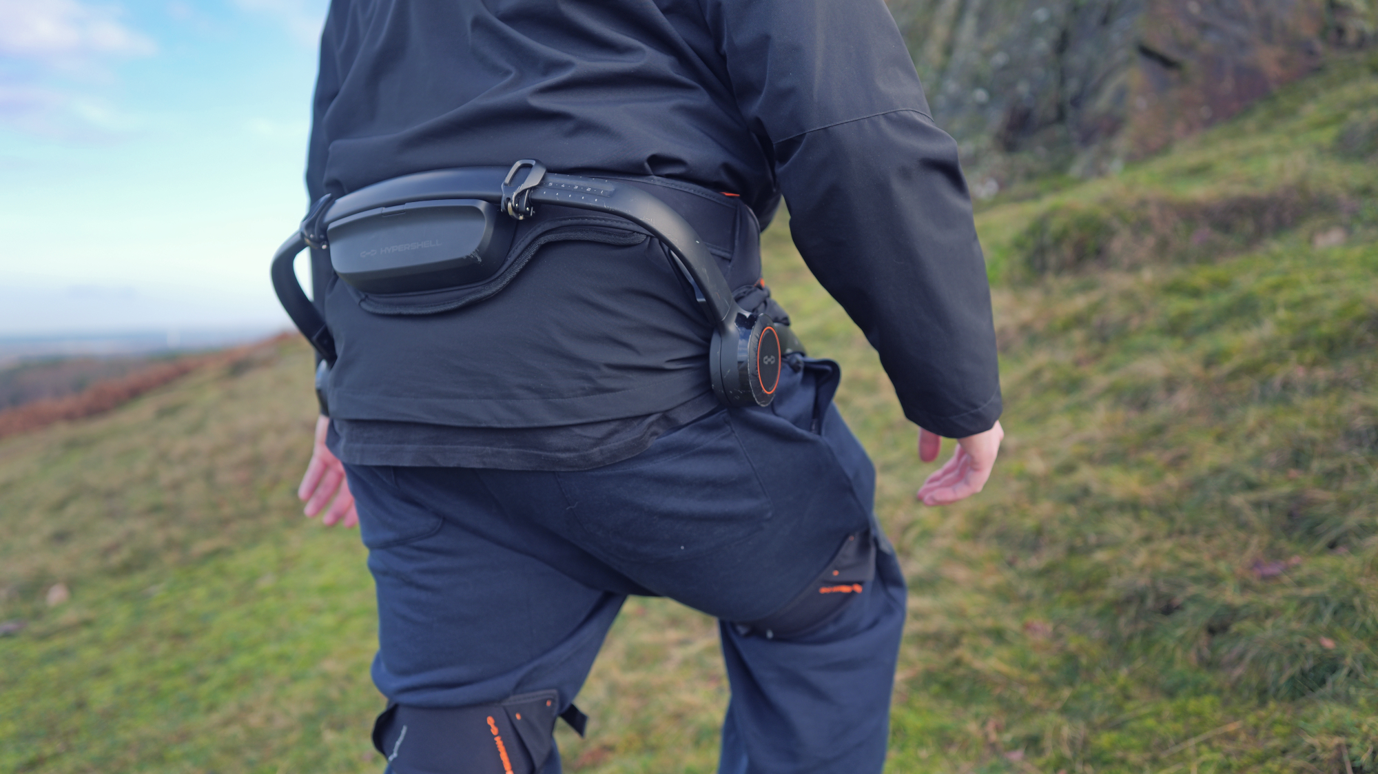 Person using a Hypershell X Ultra exoskeleton on a grassy hill