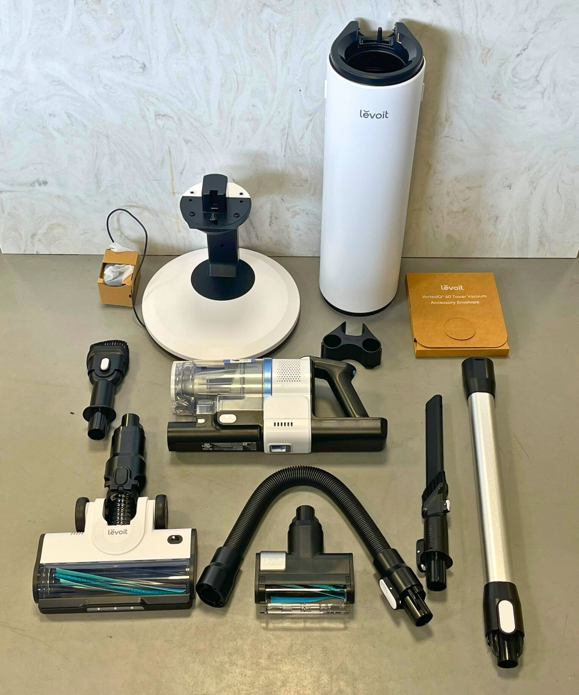 All parts of the Levoit AERO cordless vacuum laid out on gray floor in front of marble counter.