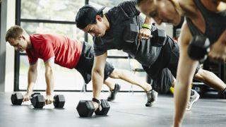 Group of friends doing renegade rows together with dumbbells in gym