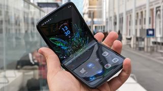 En halvt ihopvikt Motorola Razr från 2022 ligger i en hand med en stadsmiljö i bakgrunden, med mobilen vänd med skärmen mot kameran.