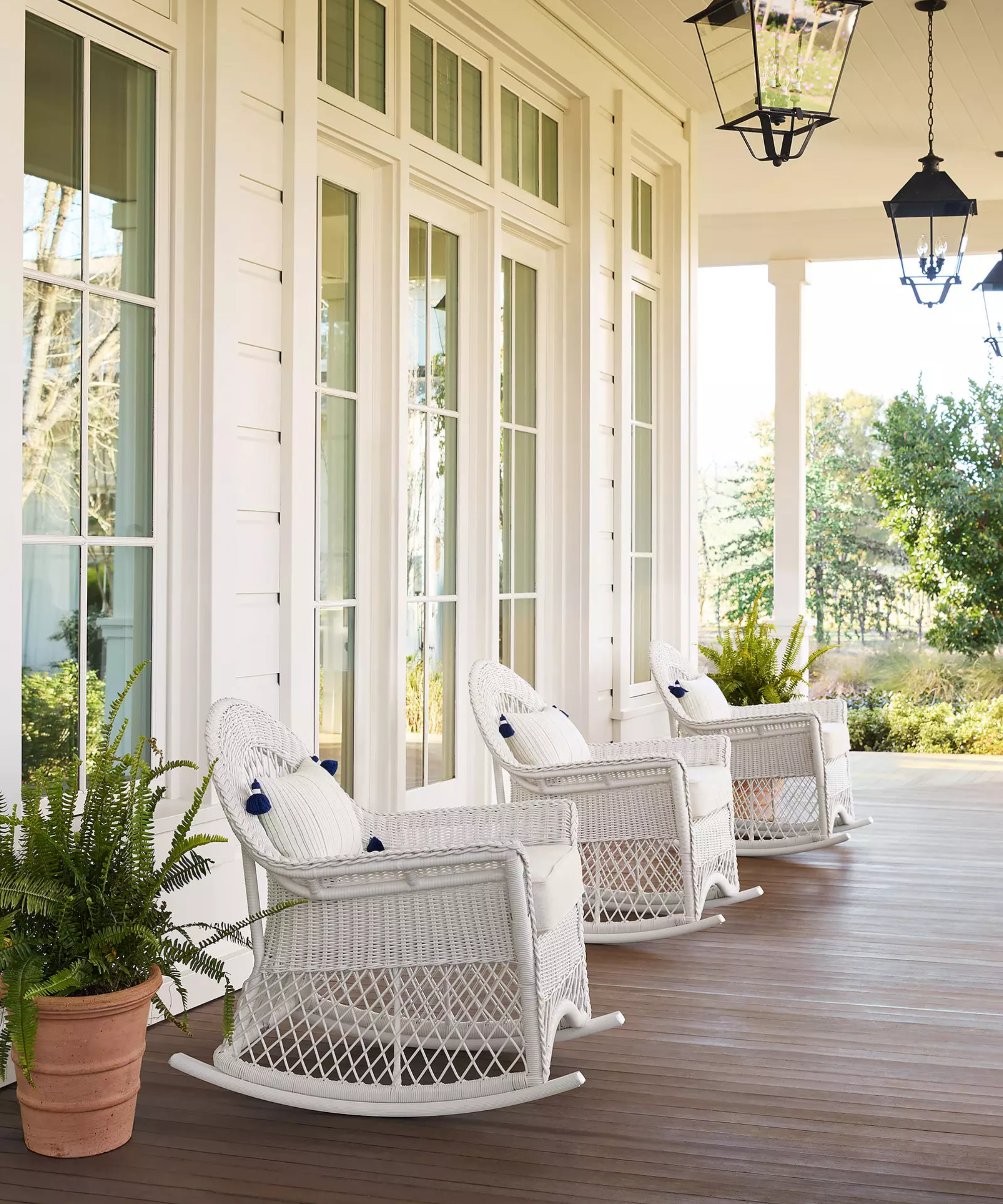 a porch with three white wicker rocking chairs