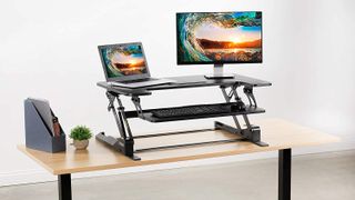 Best standing desks: The VIVO Height Adjustable Standing Desk Converter in black placed on a light wood table
