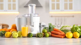 A white juicer on a kitchen counter surrounded with fruit and vegetables