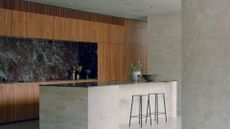 A stylish kitchen with wood cupboards, a marble backsplash, a stone island and a pair of stools