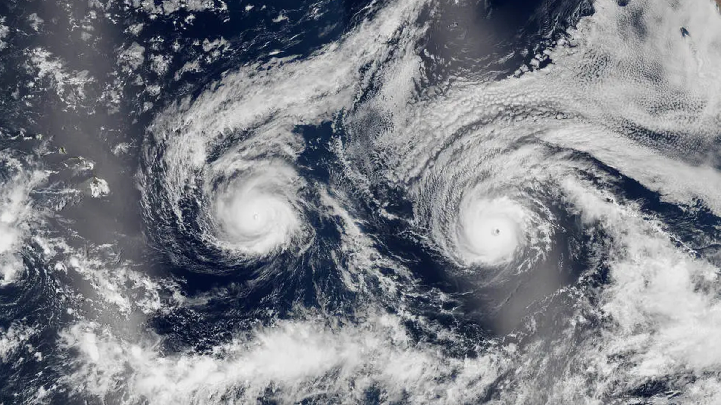 A satellite image showing two side-by-side hurricanes with swirling clouds. Collectively, the weather front looks like a smiley face