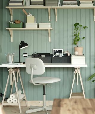 home office space with light green panelled wall, pale wood shelves and white desk