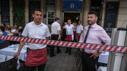 Restaurant workers stand guard over diners during a protest against overtourism in Barcelona