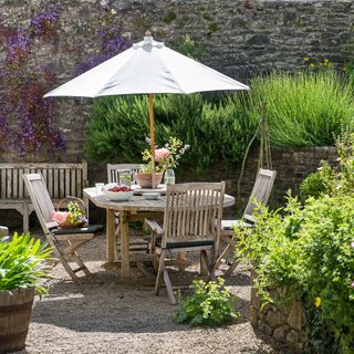 rustic outdoor dining table and chairs with parasol in pretty summer garden