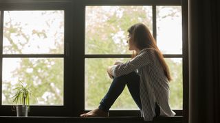 A woman sitting and looking out of a window to the outside