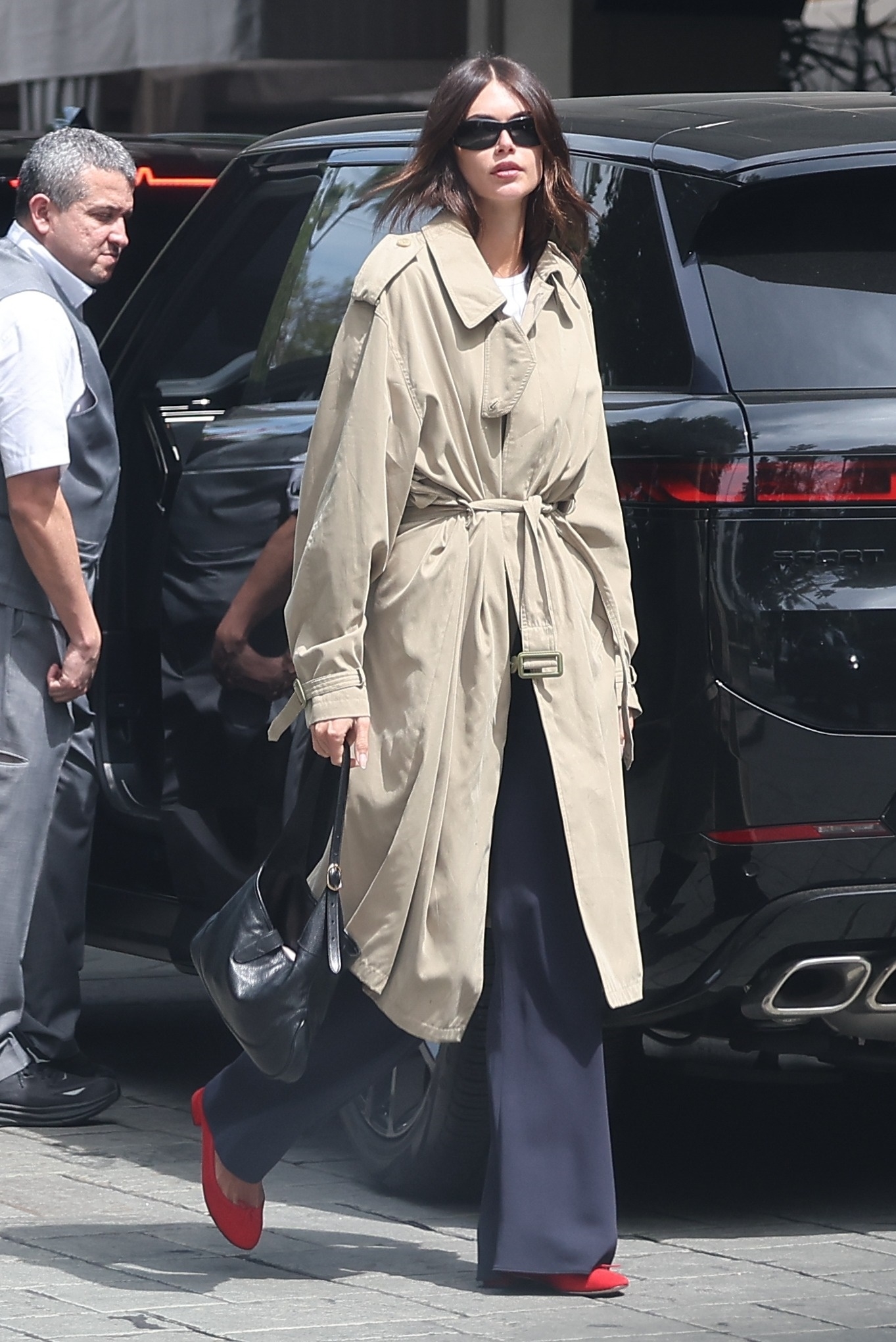 Kaia Gerber wearing a trench coat, trousers, and ballet flats