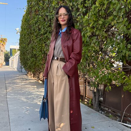 Sophie Lopez wearing a burgundy leather trench coat, a sweater, tailored trousers, and heels