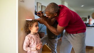 A father measures his children's height against a wall.