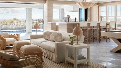 An open-concept living space where a tailored linen sofa and rattan lounge chairs meet a custom light-oak pool table, all set against a backdrop of dunes and sea.
