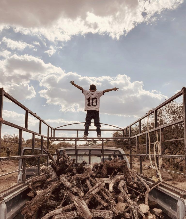 Photograph titled "Heroe," showing a young boy in a Lionel Messi football shirt standing with arms outstretched atop a flatbed truck's enclosure, shot on iPhone 12 Pro in Arandas, Jalisco, Mexico.