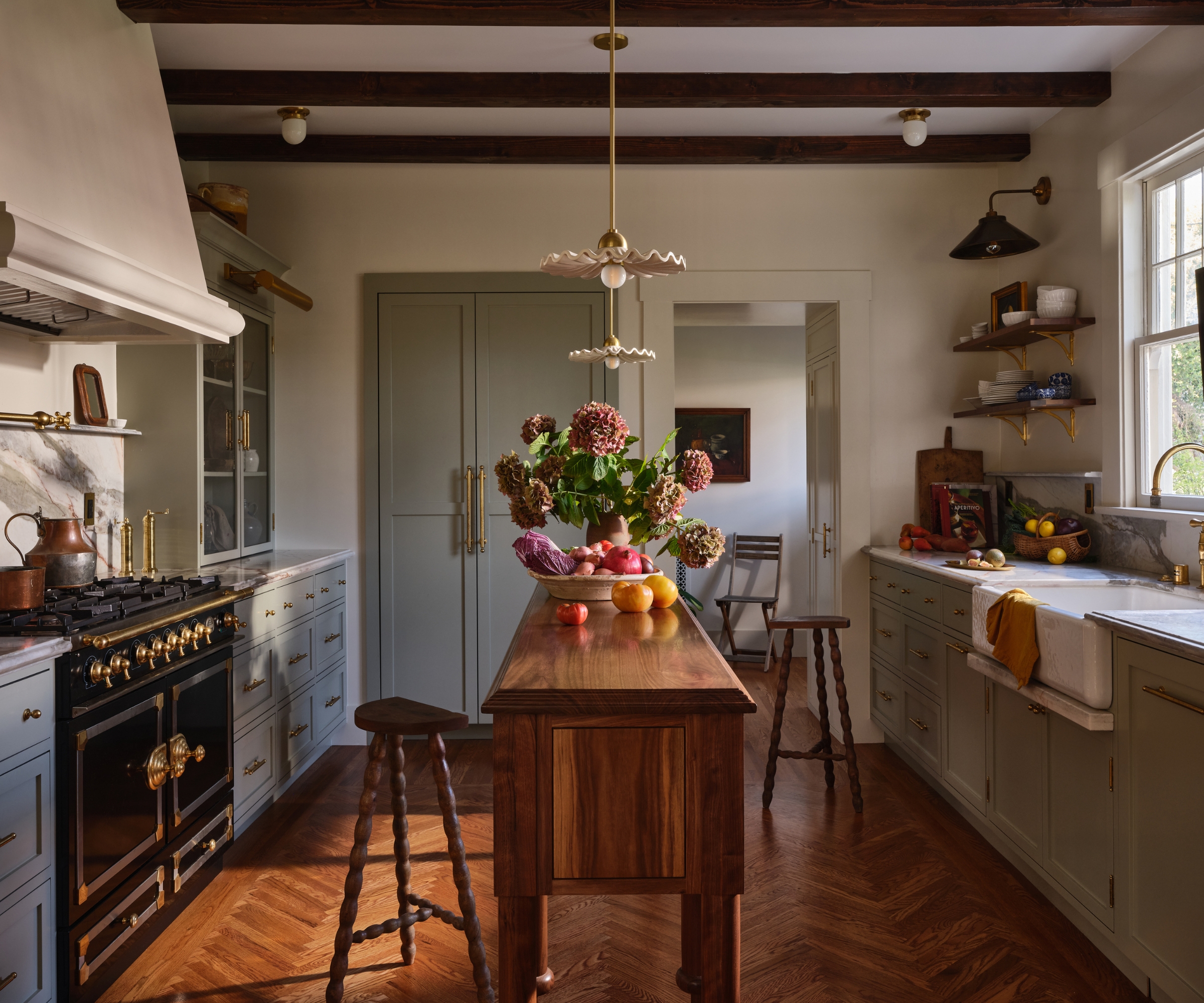 A galley kitchen with soft blue cabinets. warm white walls, and a custom narrow wooden island to perfectly fit the room