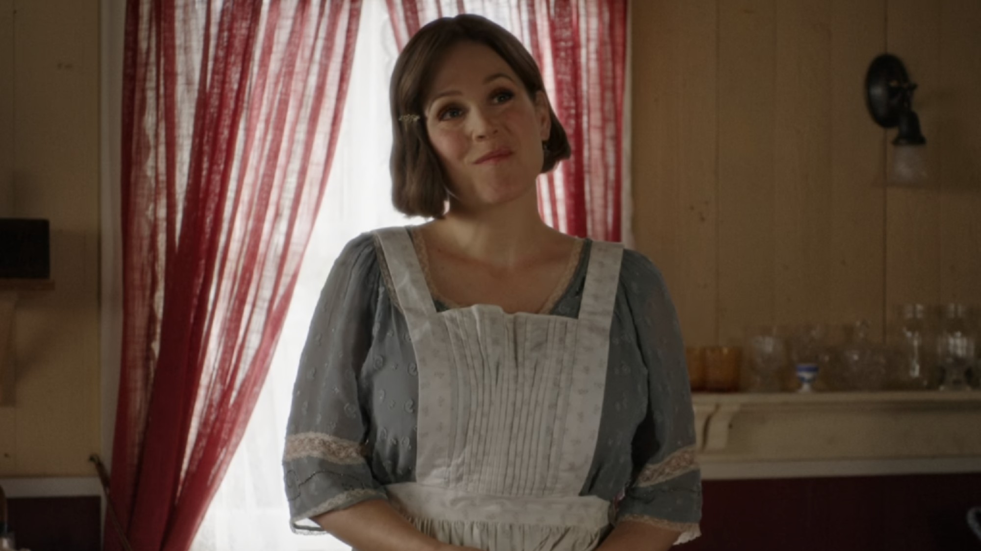 Elizabeth wearing an apron and tilting her head while smiling on When Calls the Heart.