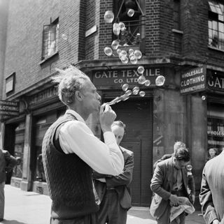 Black & white photo- a man blowing bubbles in London 1953 outside a shop