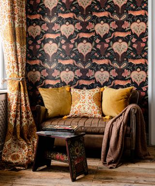 Richly patterned gold and white cushions on a small sofa with plush matching drapes in a living room with black and orange fox print wallpaper.