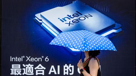 A pedestrian holding a blue polka-dot umbrella walks past a large Intel Xeon 6 processor advertisement during preparation for COMPUTEX 