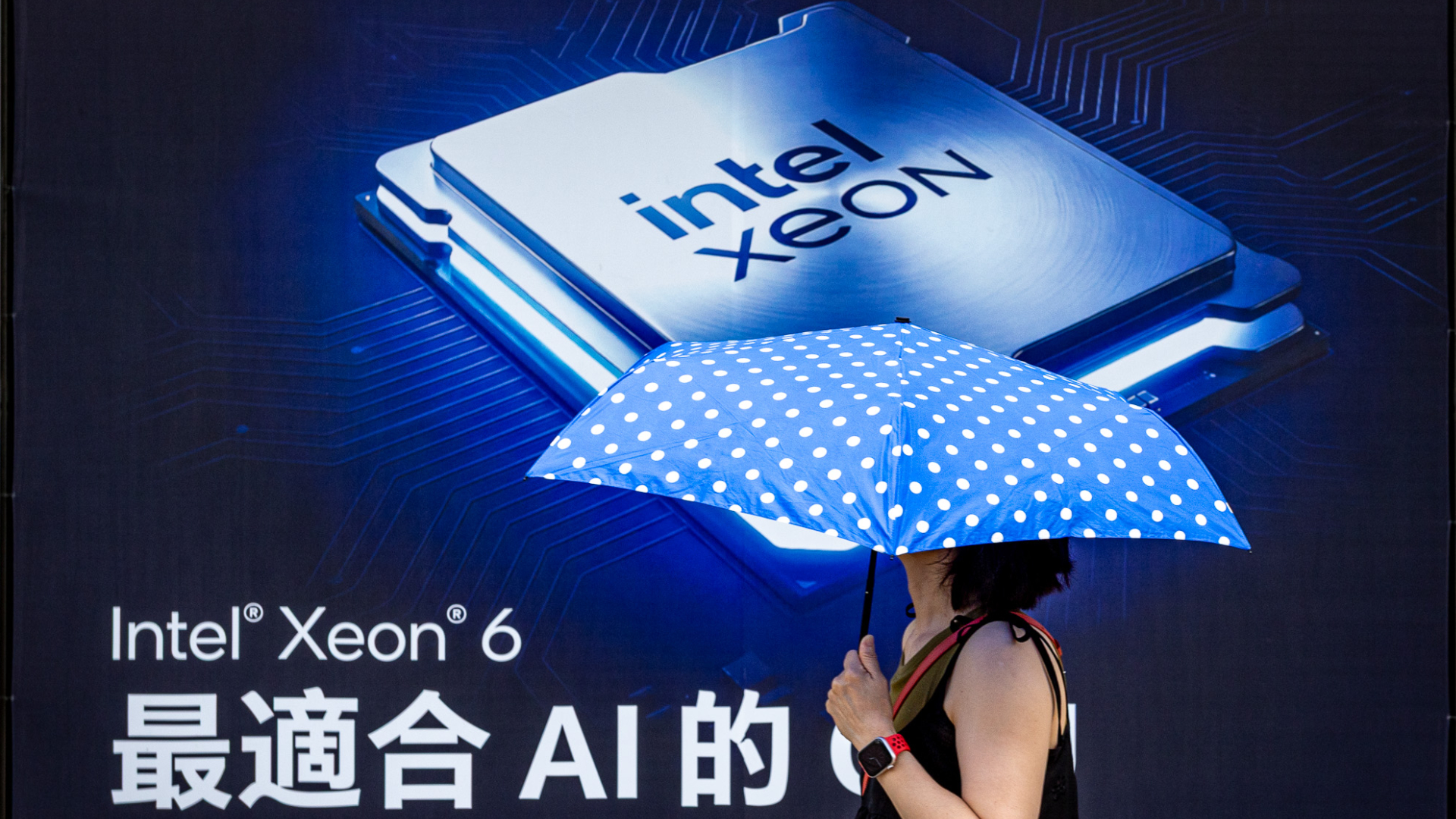 A pedestrian holding a blue polka-dot umbrella walks past a large Intel Xeon 6 processor advertisement during preparation for COMPUTEX 