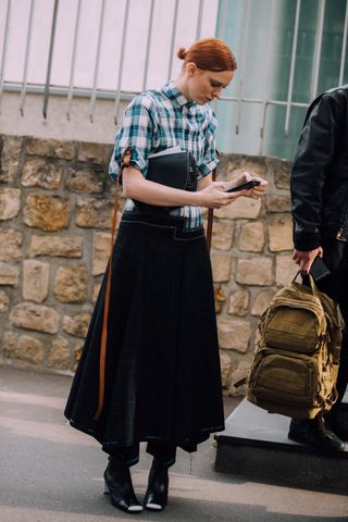 Model Karen Elson checks her phone after the Loewe show and wear a Loewe bag and plaid top denim bottom dress with black boots during Paris Fashion Week Spring/Summer 2019 on September 28, 2018 in Paris, France.