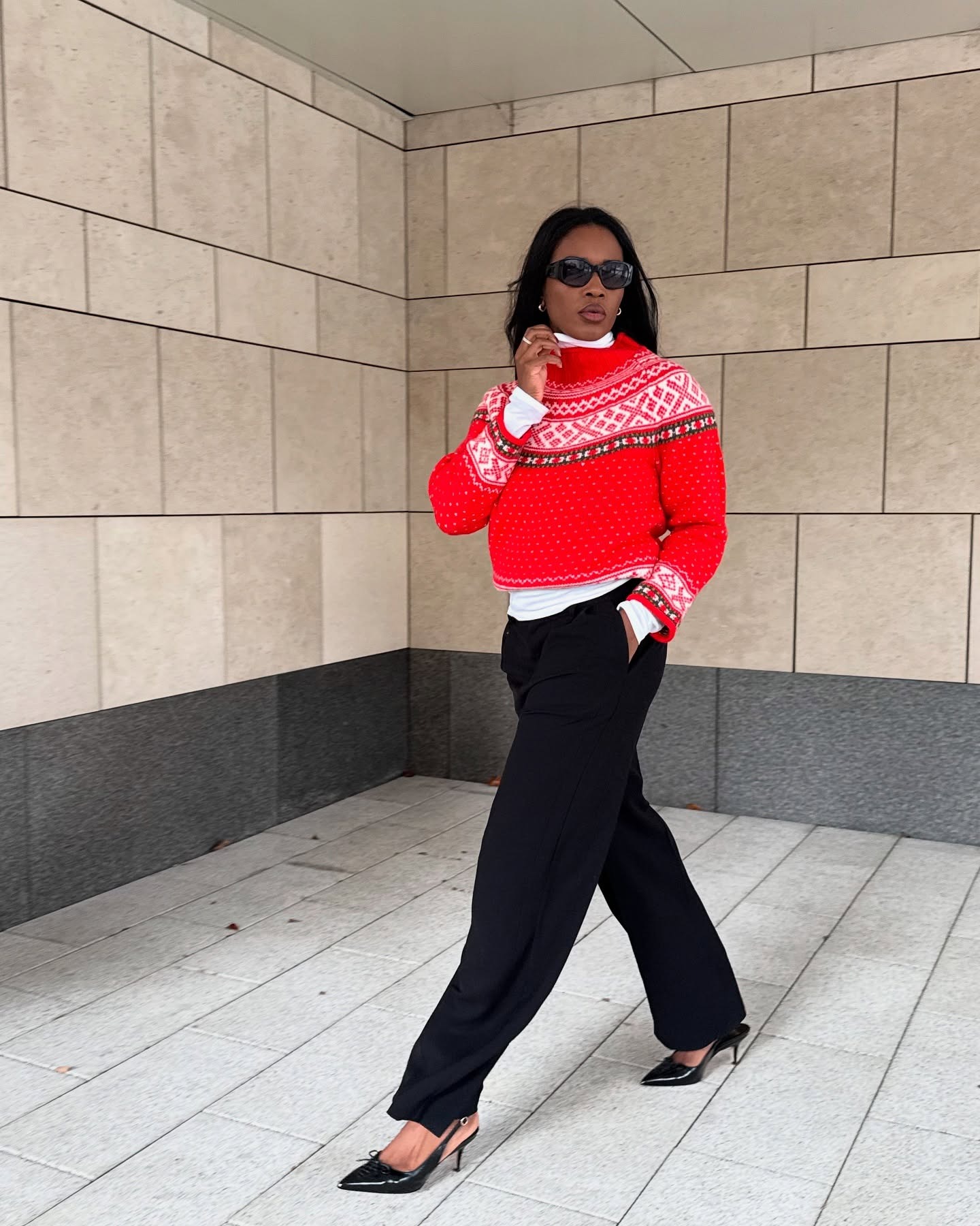 Marilyn NK is wearing a red Fair Isle crewneck sweater over a white shirt with black pants and slingback heels.