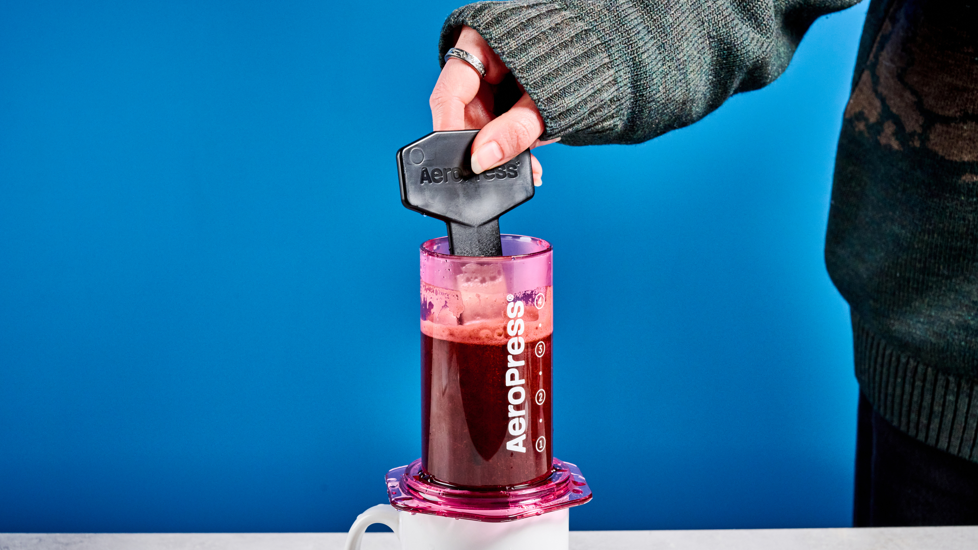 the aeropress clear color in pink photographed against the blue tom's guide background