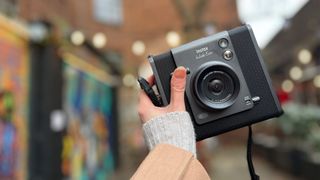 A hand holds the Instax Wide Evo