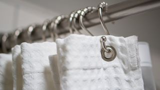 White shower curtain hanging on silver curtain rings on a silver pole.