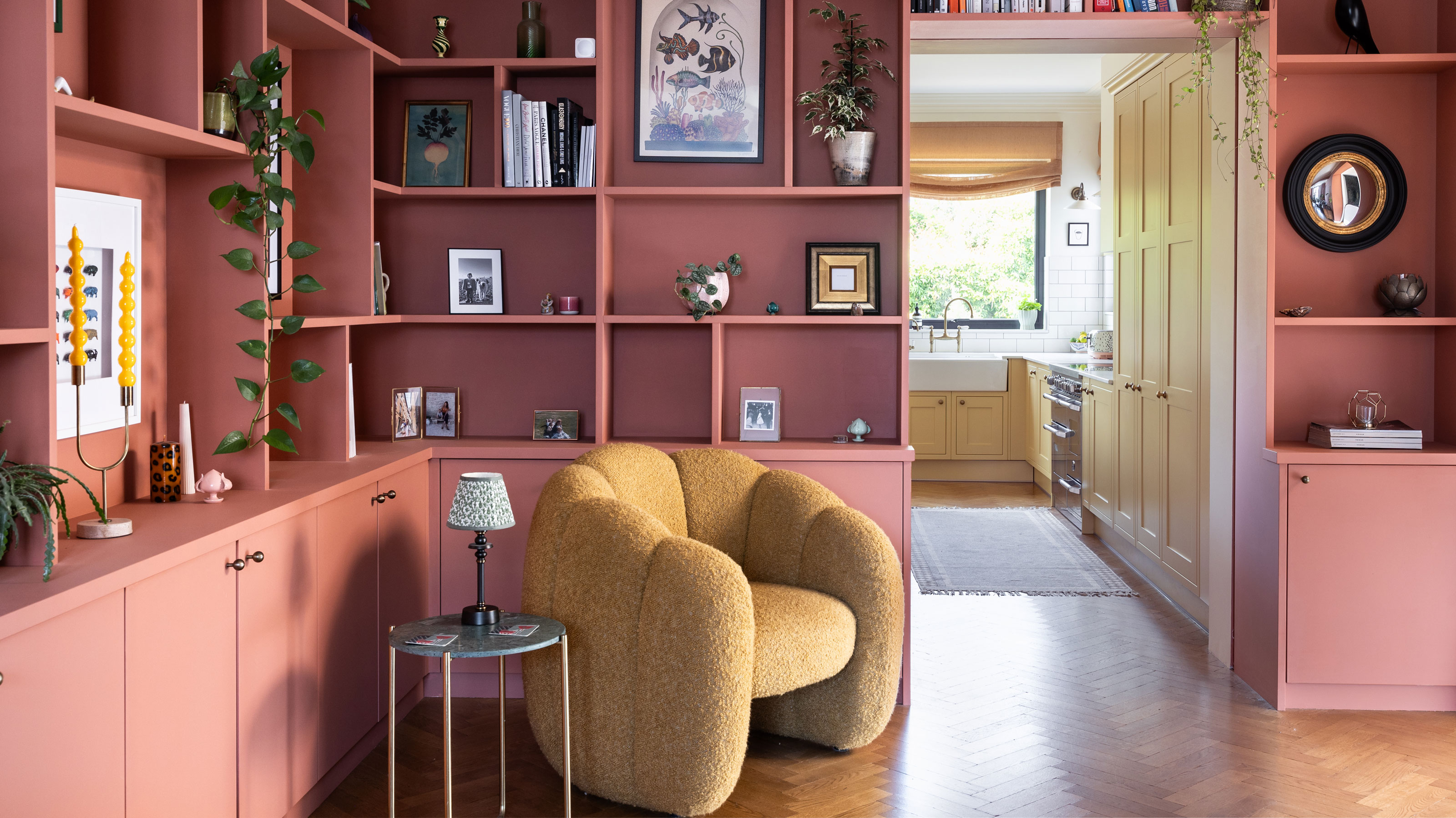 Built in shelving painted pink with a yellow scalloped armchair and a side table with rechargeable table lamp