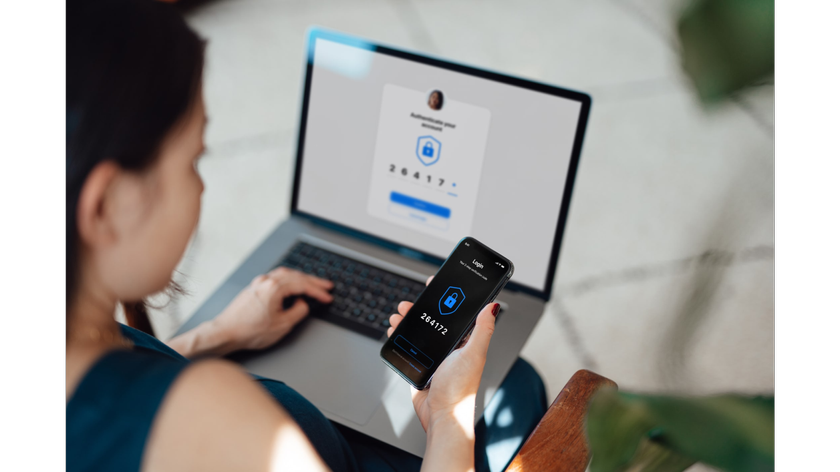 Over the shoulder view of young Asian woman using laptop, logging in online banking account with digital security mobile device at office. Internet security and digital privacy protection concept. Two-Factor Authentication (2FA) concept.