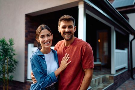 A couple hugs and poses in front of their home, or in the backyard.