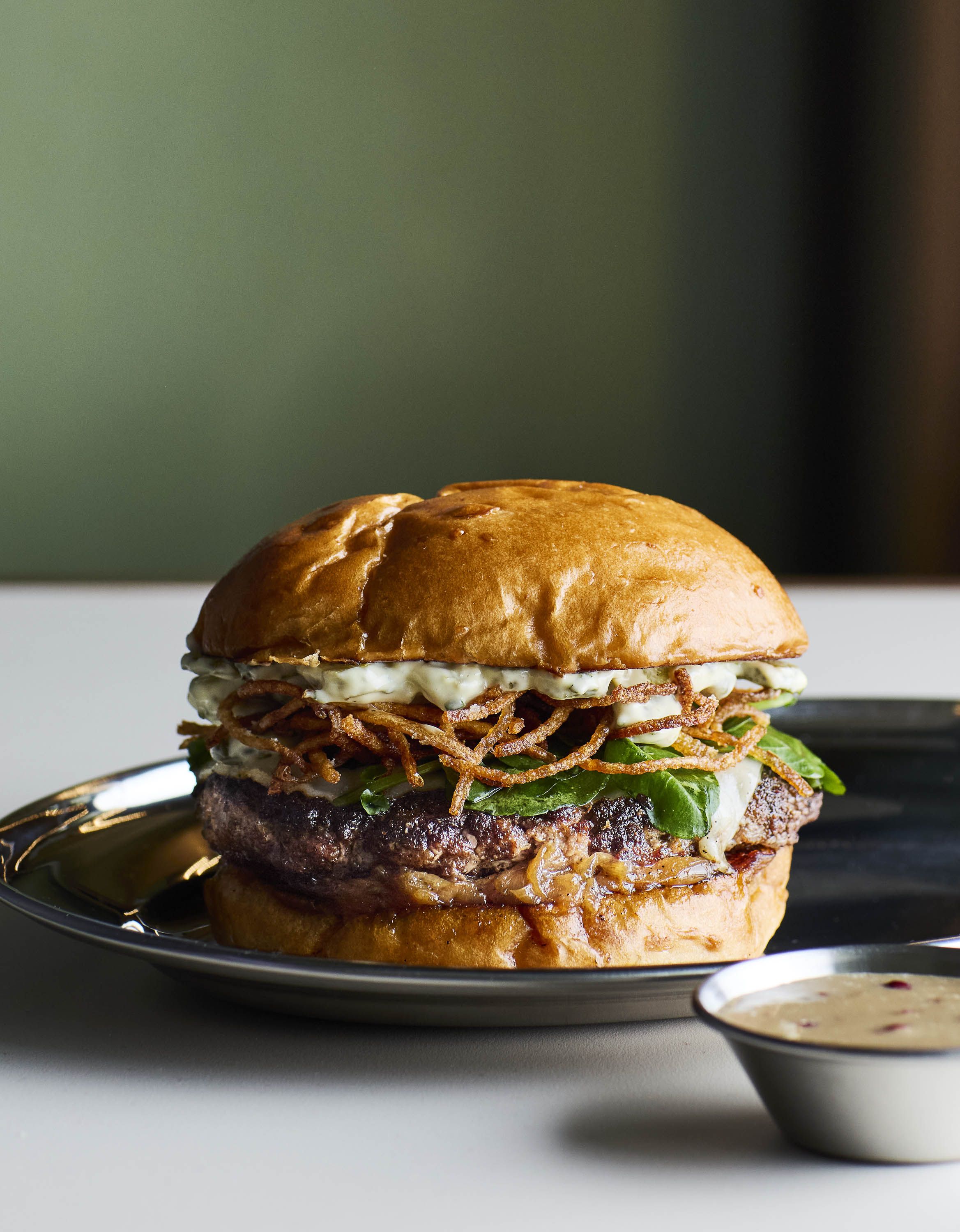 A chic burger restaurant with tiled floors, spherical art deco lighting, and ochre and green tiling.