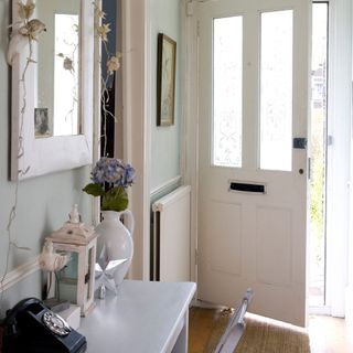A small hallway in white and light blue with a wall mirror and radiator